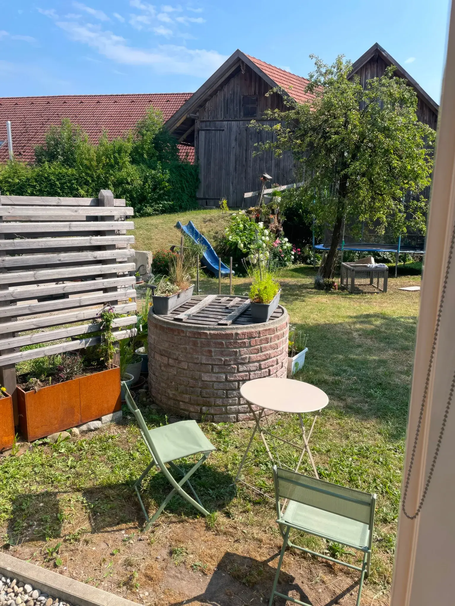 Garten der Ferienwohnung Klärle in Leutkirch im Allgäu mit gemauertem Brunnen, Rutsche und Trampolin