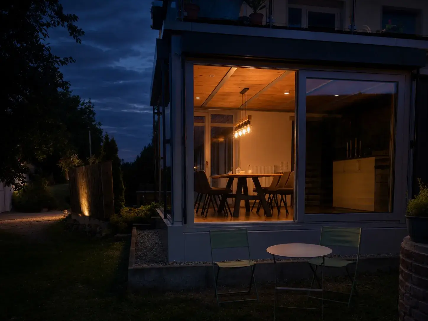 Ferienwohnung Klärle in der Abenddämmerung, der beleuchtete Wintergarten leuchtet in den Garten
